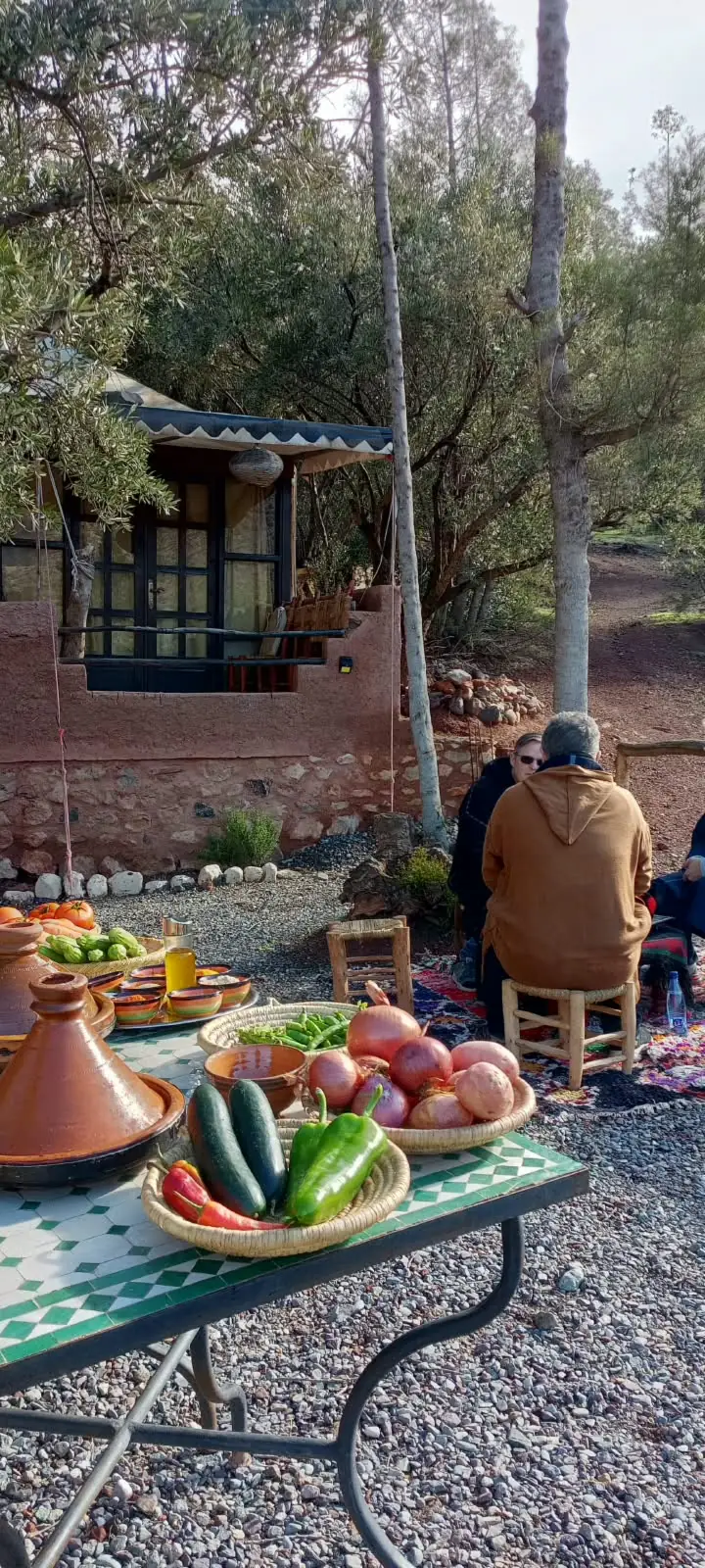 Table d'atelier avec tajines en terre cuite et légumes frais, sous les arbres