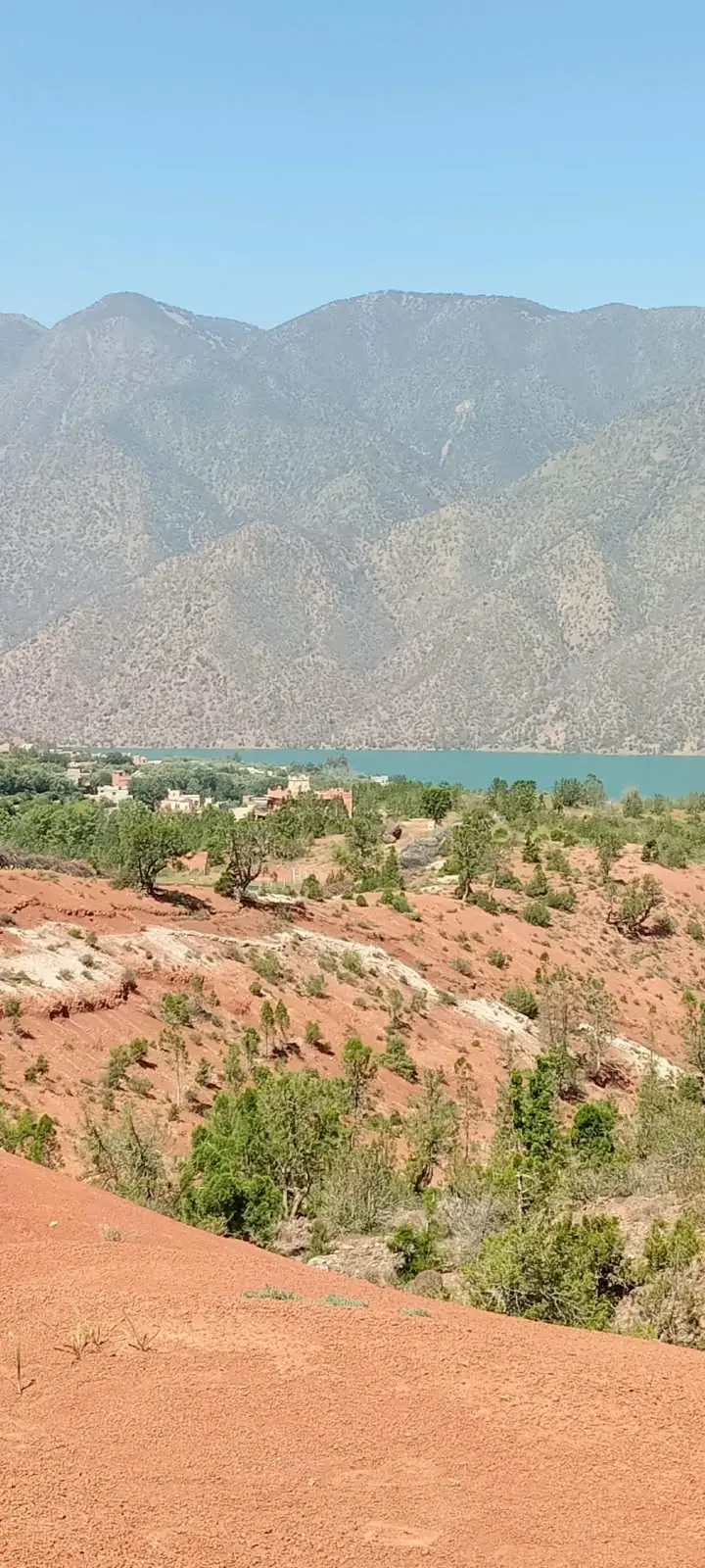 Collines de terre rouge descendant vers le lac d'Ouirgane, montagnes au loin